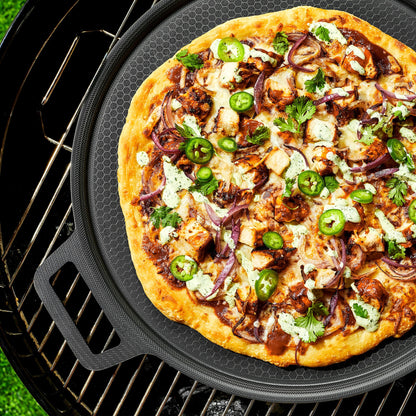 A pizza with veggies and chicken on the HexClad hybrid pizza steel, sitting on a grill