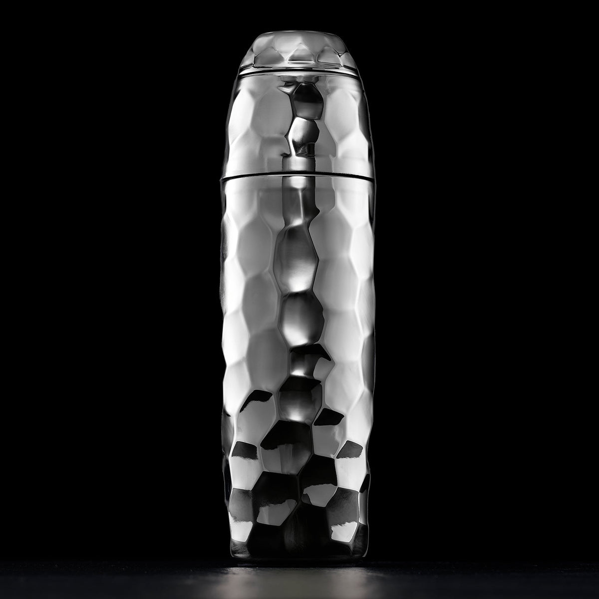 Metallic chrome, hexclad cocktail shaker with a textured surface on a black background